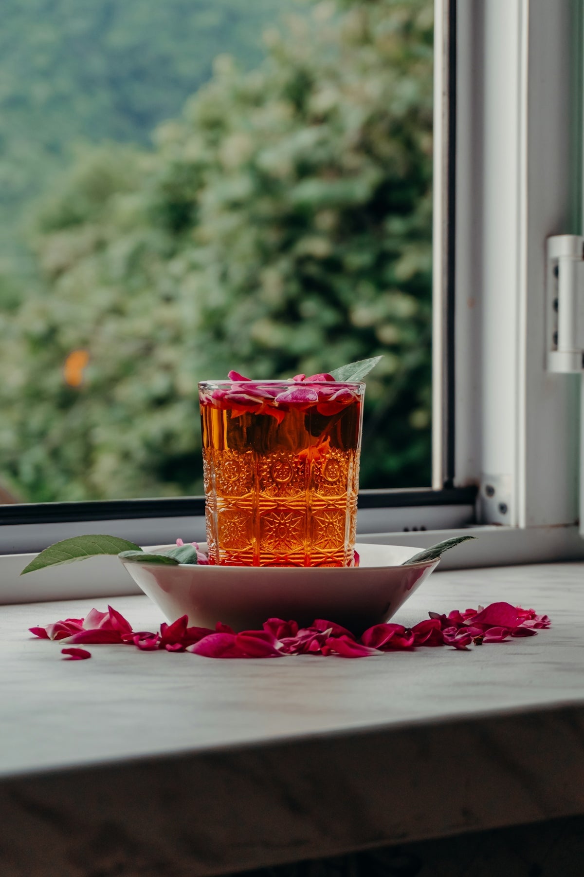 Glass of amber liquid with rose petals and leaves.